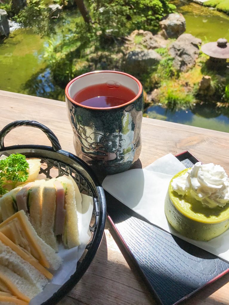 A cup of Hojicha with a tray of tea sandwiches and Green Tea Cheese Cake overlooking the pond at the Japanese Tea Garden in San Francisco